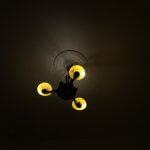 A dark ceiling illuminated by an old fashioned light fitting with 3 glass lampshades