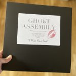 Black master bag sleeve with a white stick that says Ghost Assembly is a font similar to Vogue magazine. There is a lip print on the sticker.